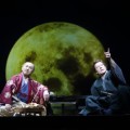 two characters sit before a backdrop of the moon at night
